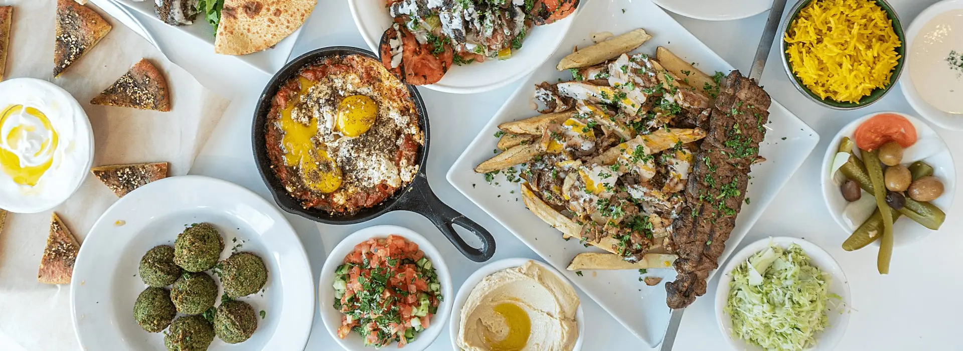 A table covered with PITA 22 dishes: shakshuka, falafel, shawarma fries, kabob, hummus, rice and salads