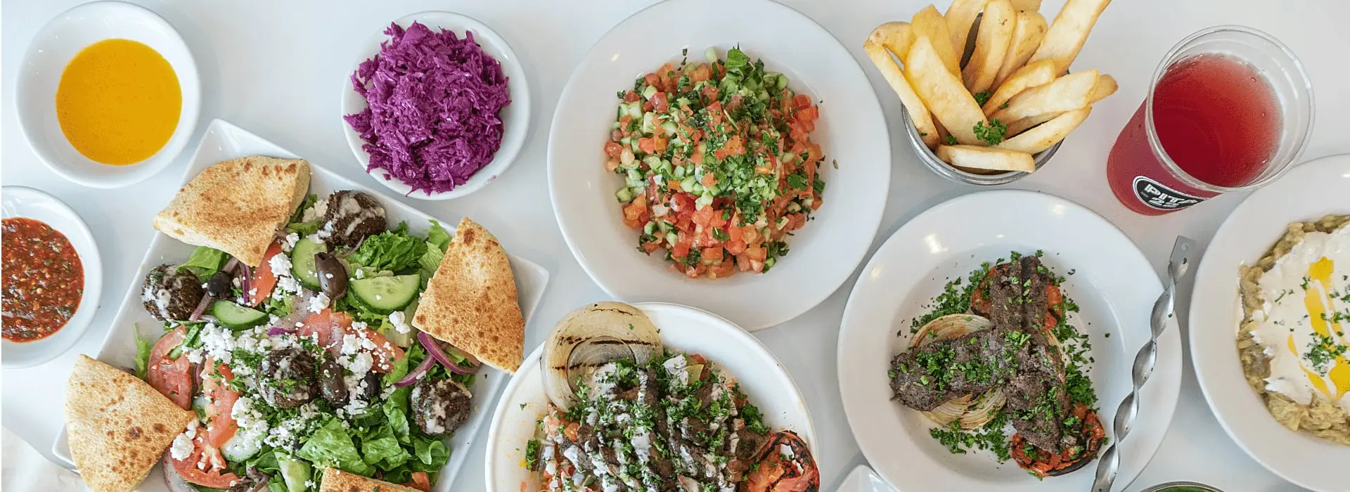 Greek salad with falafel, chopped salad, kabobs, fries and dips on a white table